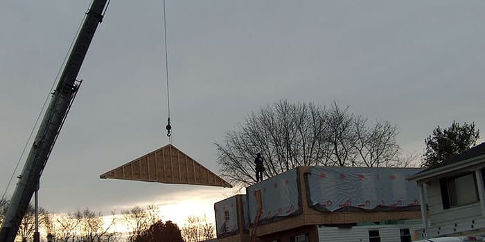 crane bringing a piece of wood over to a worker on top of a house