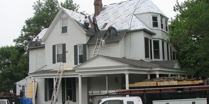 multiple workers on the top of a large house working on roofing
