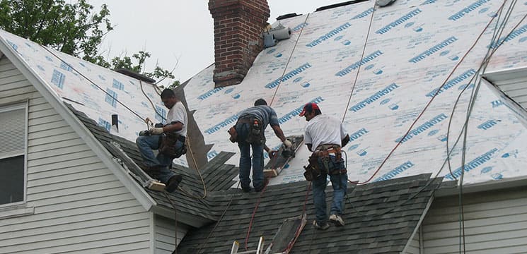 three workers on roof working on shingles for roofing