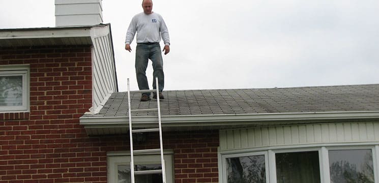 worker walking down a roof towards a ladder to continue the roofing job
