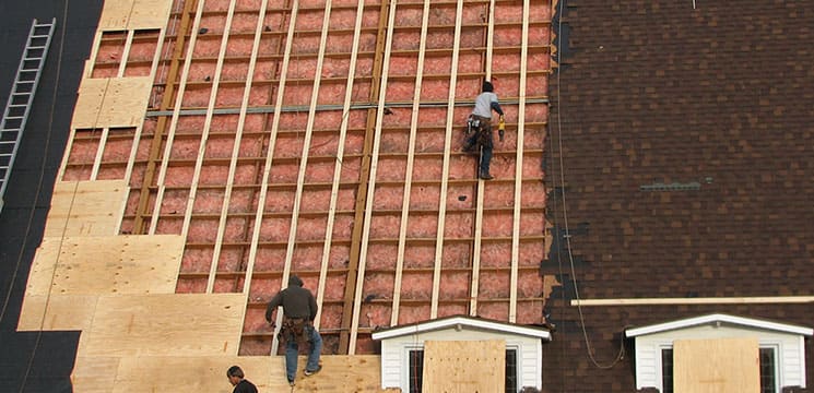 two workers on roof working on insulation and beam work for roofing
