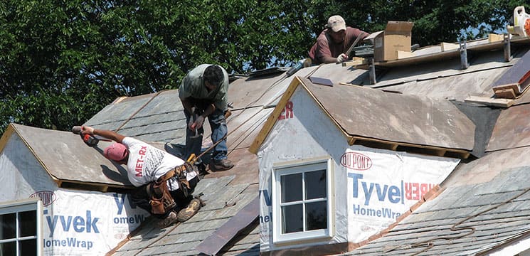 three workers on roof working on shingle roofing