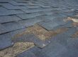 Closeup of damaged asphalt shingles on residential roof.