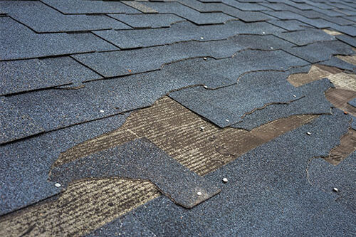 Closeup of damaged asphalt shingles on residential roof.