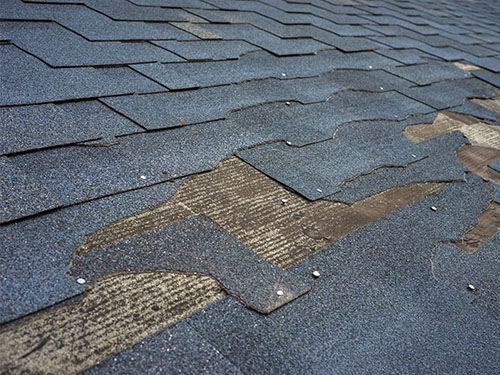 ec-oct-blog2 Closeup of damaged asphalt shingles on residential roof.