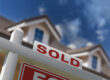 Closeup of for sale sign with home in background.