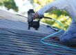 Roofing securing architectural shingles to roof using a nail gun.