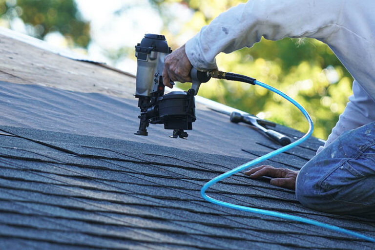 Roofing securing architectural shingles to roof using a nail gun.