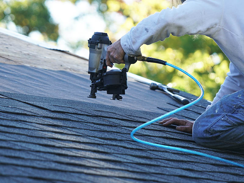 Roofing securing architectural shingles to roof using a nail gun.