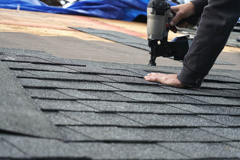 Roofing using a nail gun to secure new shingles to a roof.