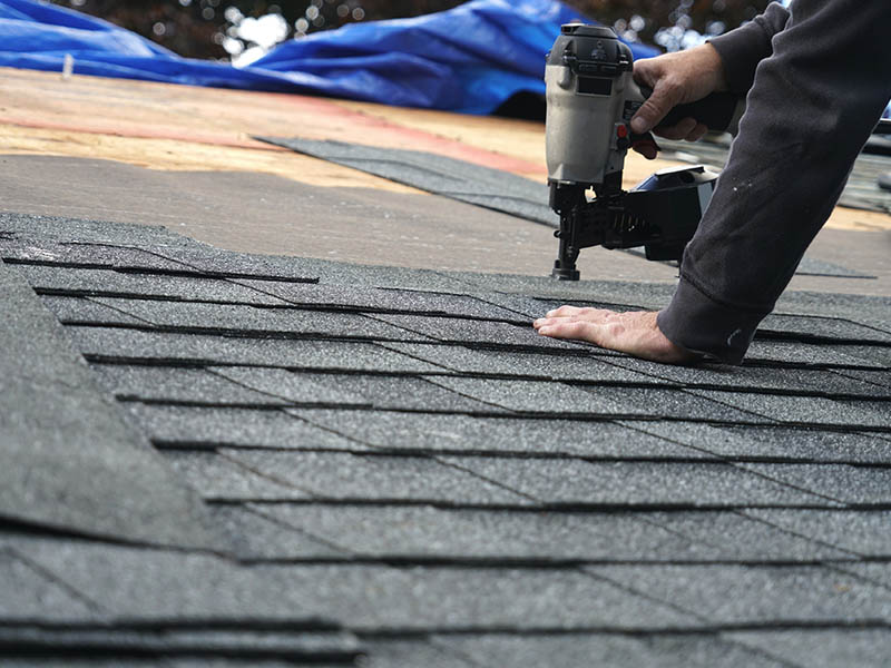 Roofing using a nail gun to secure new shingles to a roof.