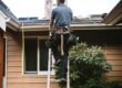 Male roofer climbing up a ladder to a residential roof.