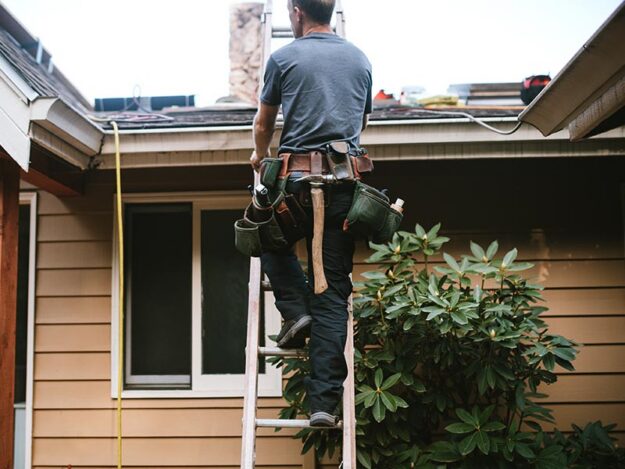 choosing-roofing-contractor Male roofer climbing up a ladder to a residential roof.