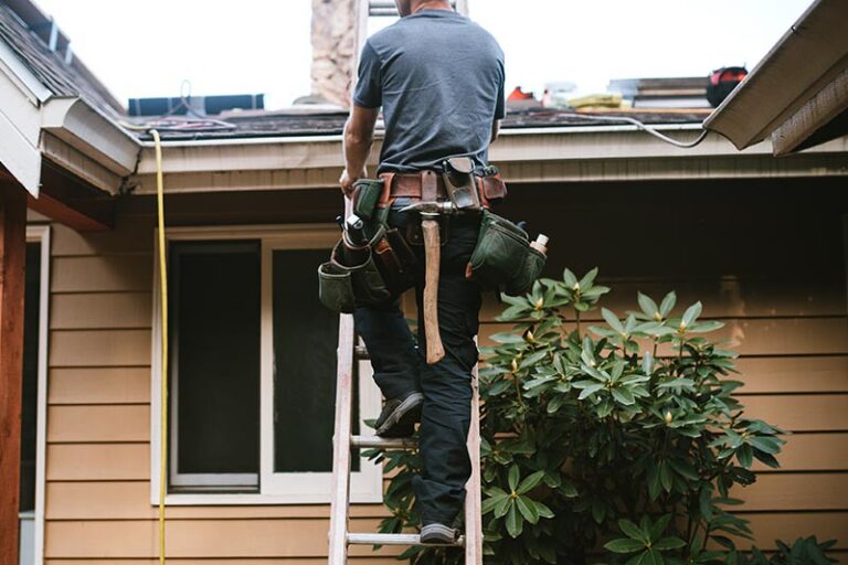 Male roofer climbing up a ladder to a residential roof.
