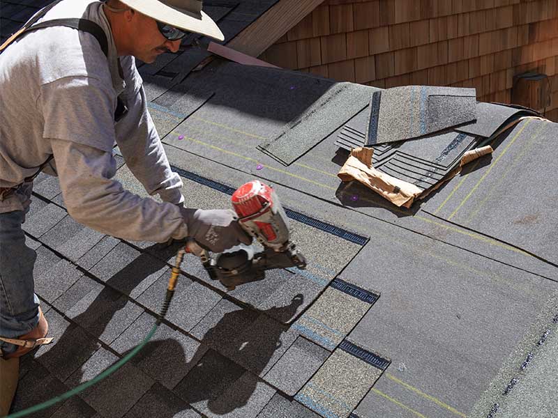 Roofer using nail gun to secure shingles.