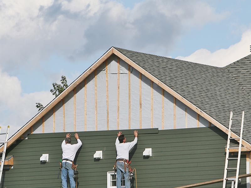 Two contractors on scaffolding placing new siding on a residential home.
