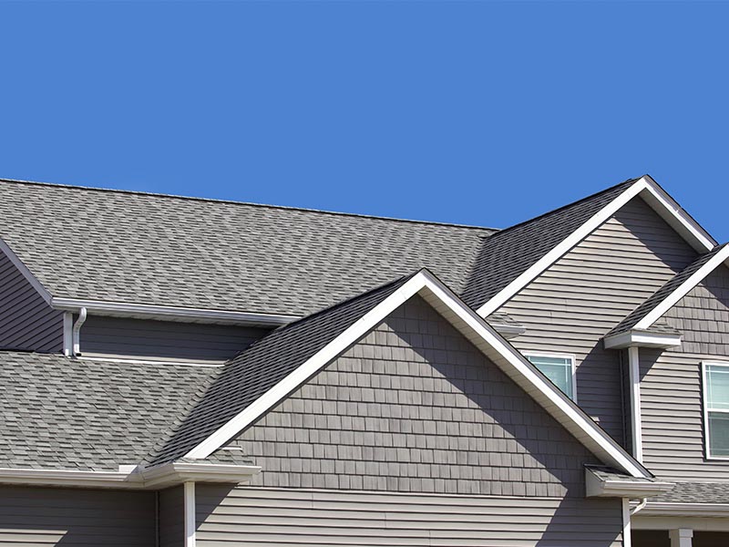 Residential home with a new gray shingle roof and blue sky visible behind it.